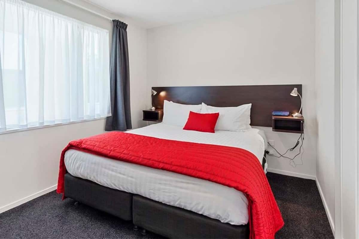 A hotel room with a bed, a nightstand, a lamp, and a window with curtains.