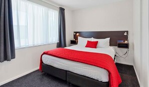 Habitación de hotel con cama, mesita de noche, lámpara y ventana con cortinas.