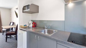 Una kitchenette compacta con microondas, tetera y lavamanos.