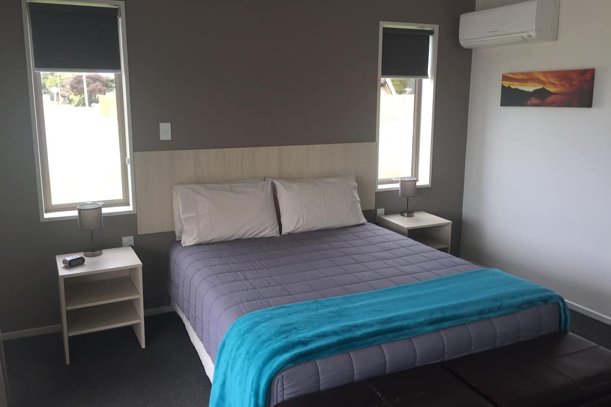 A bedroom with a bed, two bedside tables, a nightstand, a window, and an air conditioning unit.