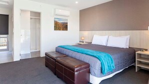 Habitación de hotel moderna con una cama grande, un banco, una mesita de noche y un cuadro en la pared.