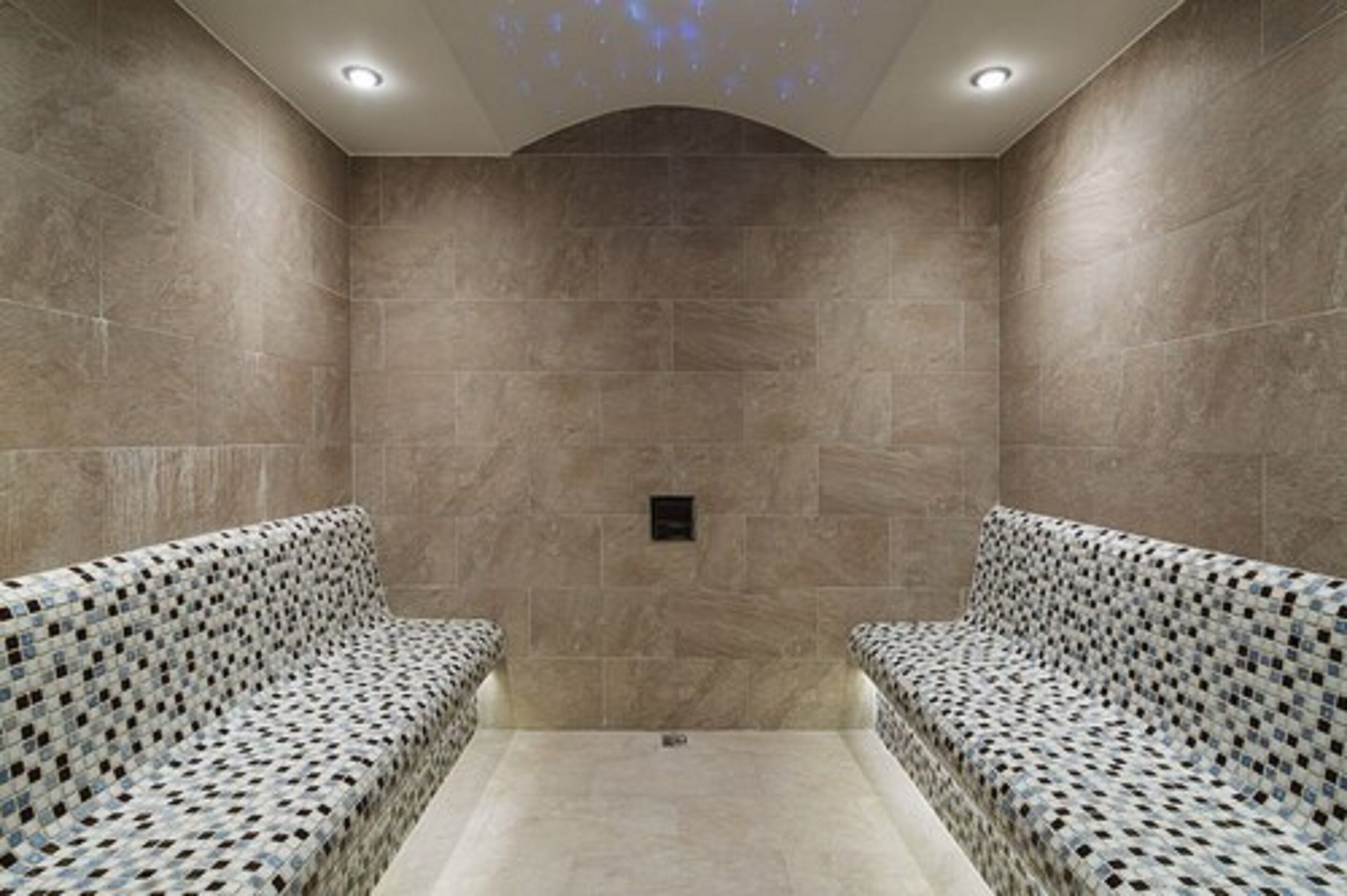 A spa room with two patterned benches, a tiled floor, and a recessed ceiling light.