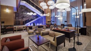 Eine großzügige Lobby mit modernem Design, inklusive einer zentralen Treppe, verschiedenen Sitzbereichen und großer Kronleuchter.