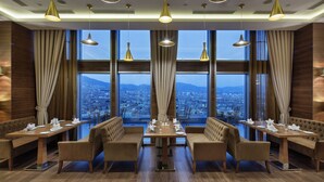 Ein Restaurant mit Blick auf die Stadt, Holzmöbeln und Pendelleuchten.