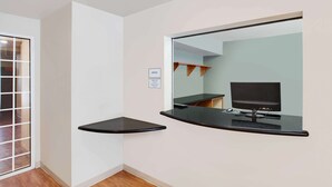 A corner of a room with a black countertop and a mirror reflecting a TV and a desk.