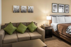 A hotel room with a sofa, a bed, a nightstand, and wall art.