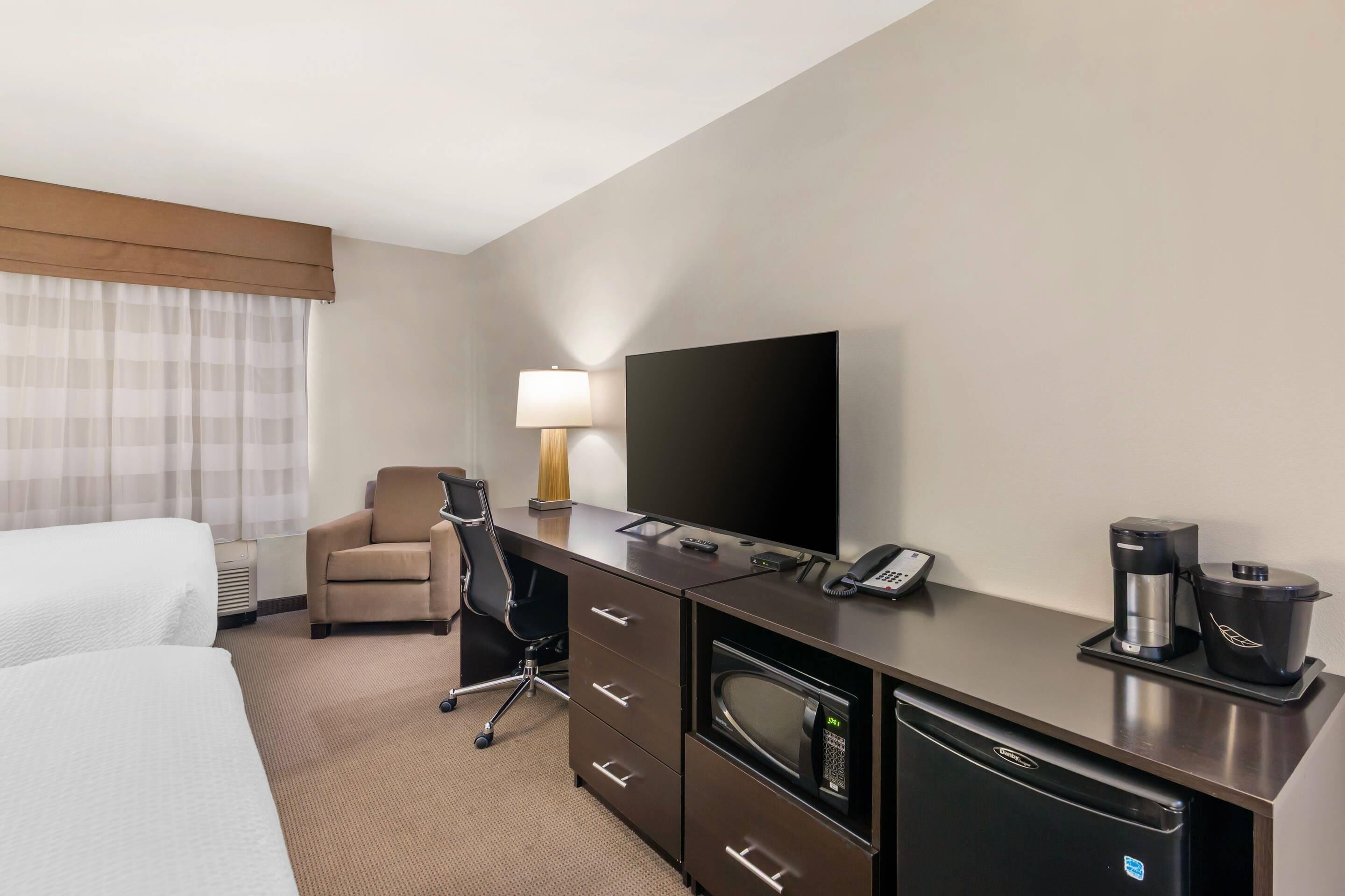 A hotel room with a bed, a desk with a lamp, a television, a coffee maker, and a microwave.