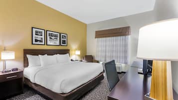 A hotel room with a large bed, two bedside lamps, a desk with a lamp, a chair, and a window with curtains.
