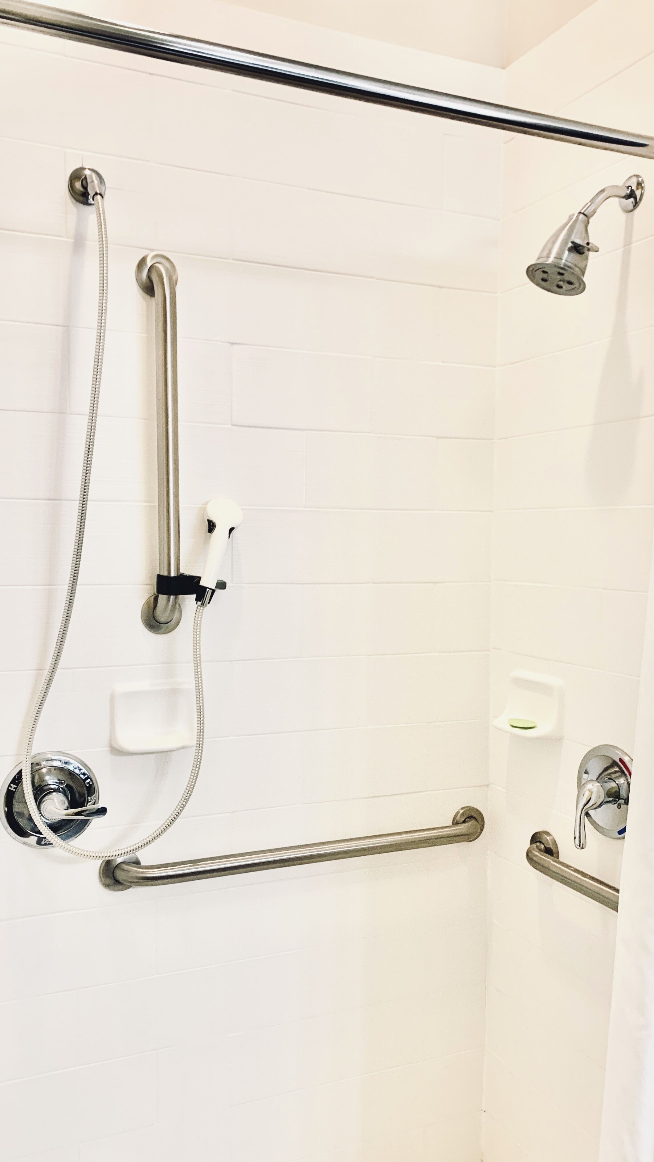 Zona de ducha con barras de apoyo, cabezal de ducha manual y grifo de pared.