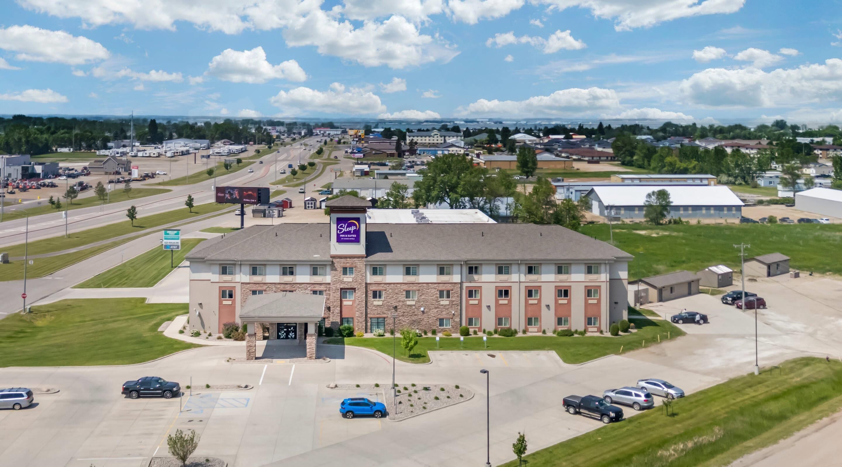 A multi-story hotel with a stone facade, a central entrance, and a parking lot with several cars.