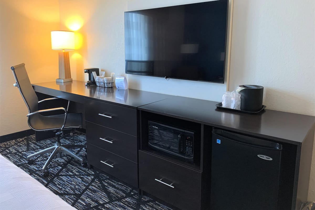 A hotel room with a desk, chair, television, and a minibar.