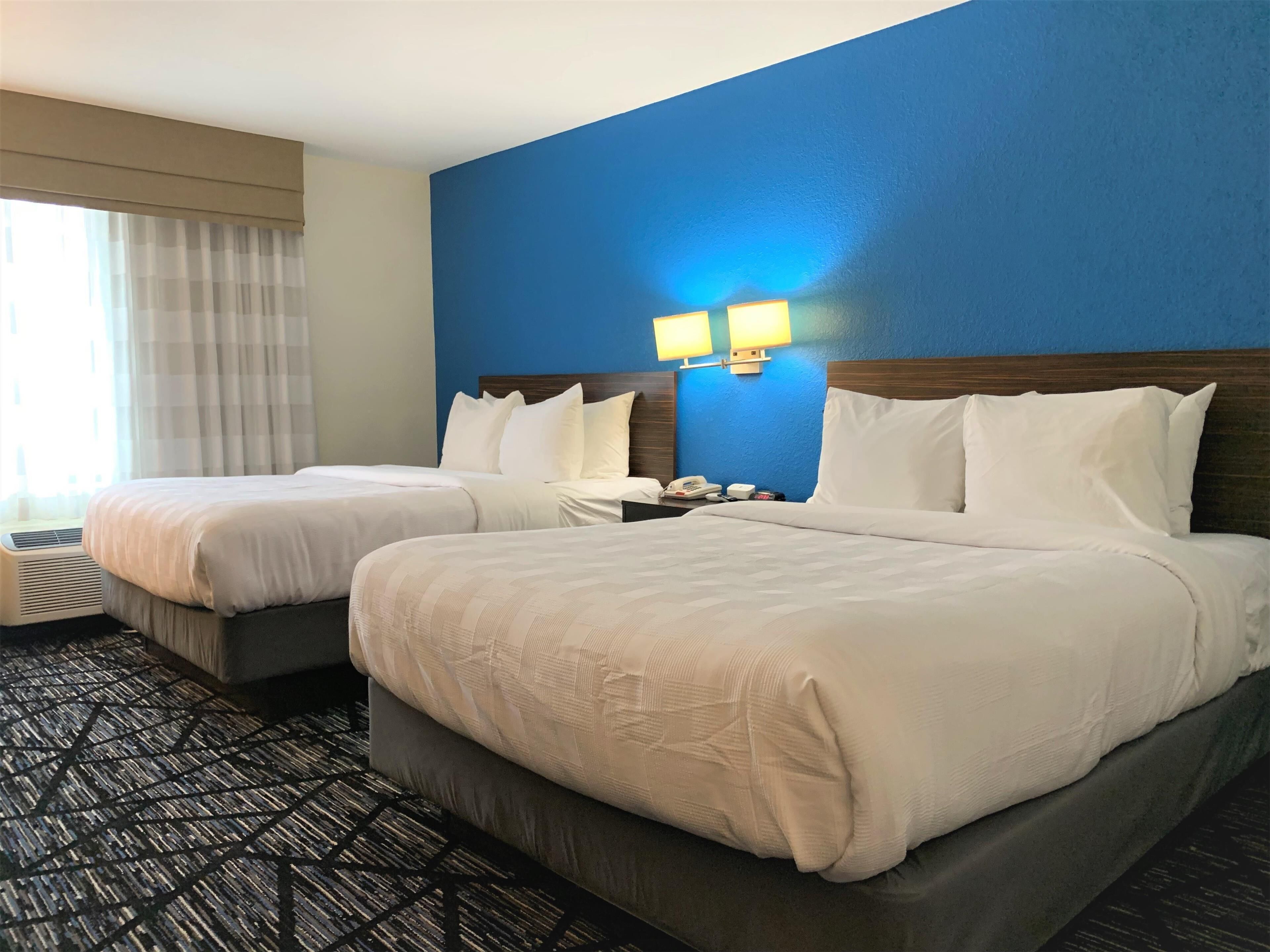 Quarto de hotel com duas camas, uma parede azul de destaque e uma janela com cortinas.