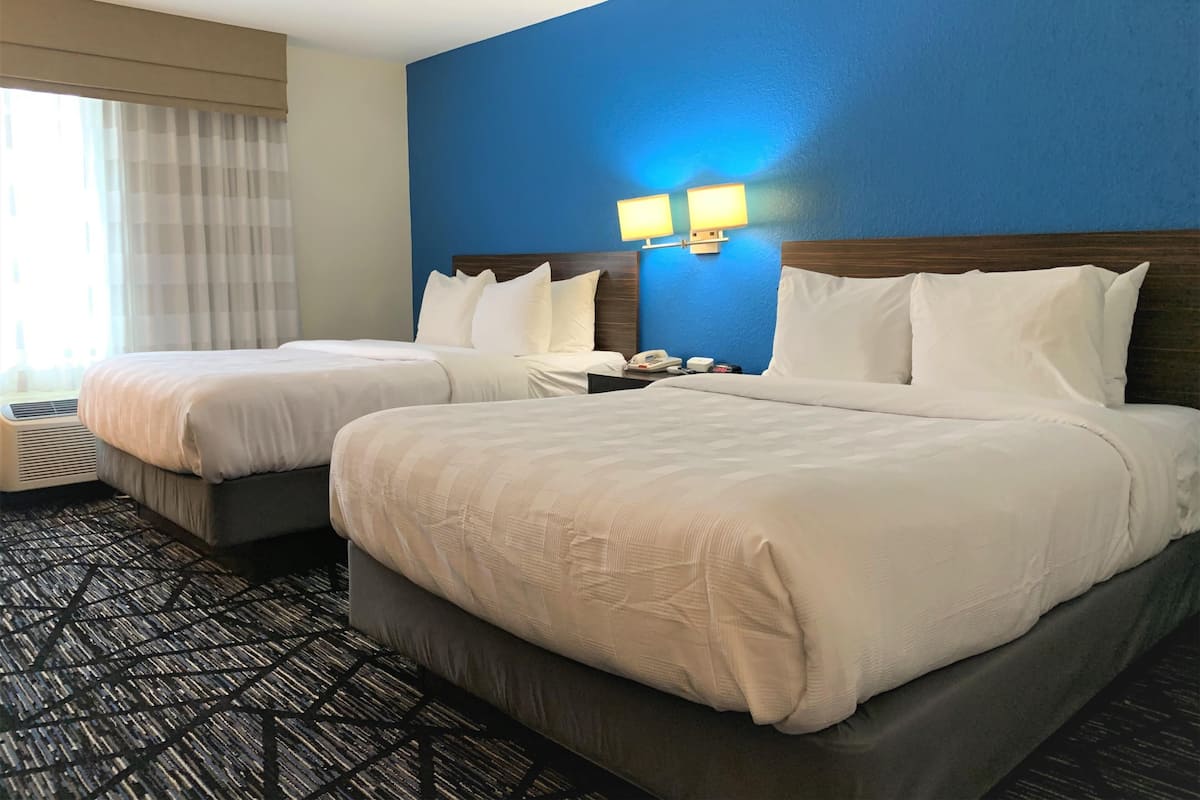 A hotel room with two beds, a blue accent wall, and a window with curtains.