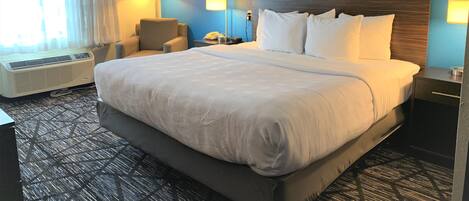 A hotel room with a large bed, two bedside lamps, a chair, a desk, and a window with curtains.