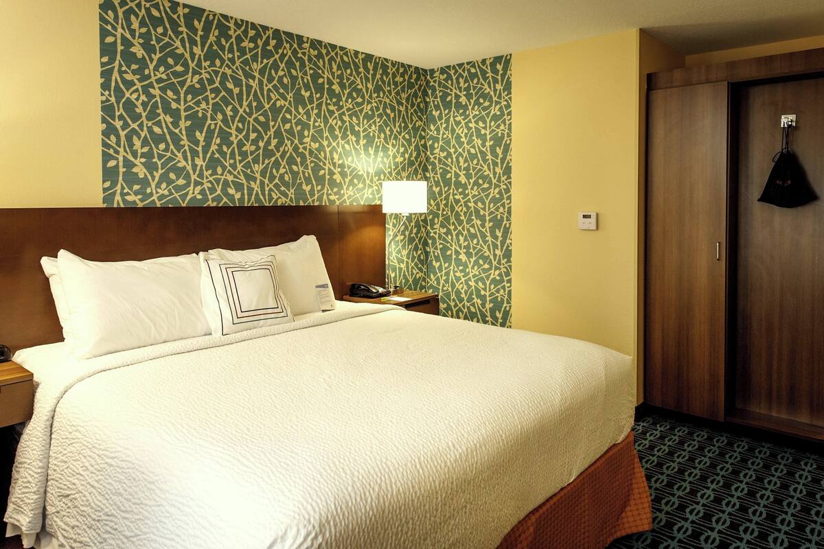 A hotel room with a large bed, a nightstand, a lamp, a wardrobe, and a patterned wallpaper.