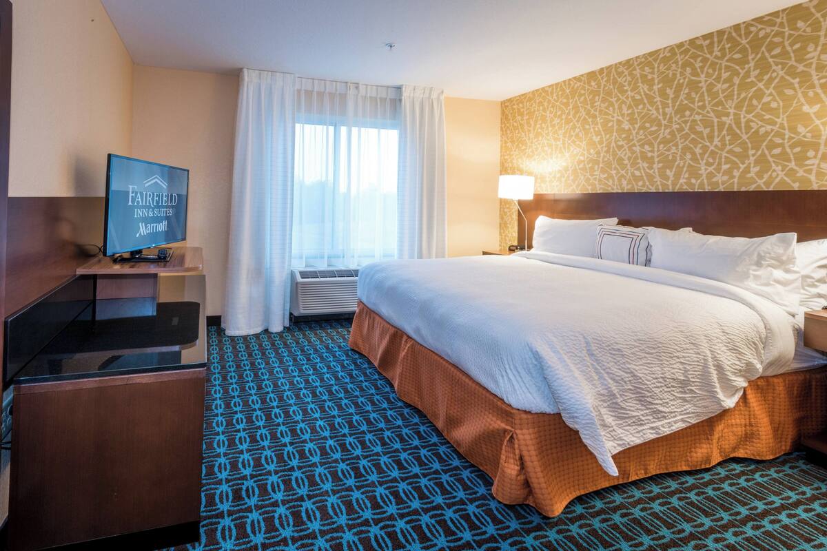A hotel room with a large bed, a television on a stand, a desk, and a window with curtains.
