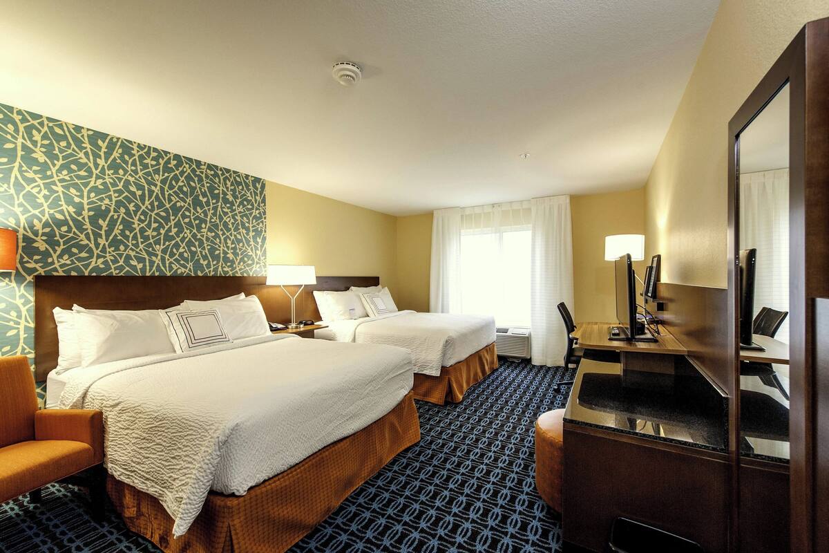 A hotel room with two beds, a desk, a chair, a mirror, and a patterned carpet.