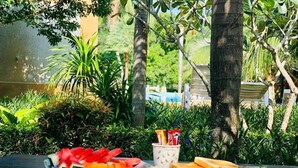 A table set outdoors with plates of food, including sandwiches and fruit, in a lush garden setting. - Peaceful Resort Koh Lanta (Ko Lanta)