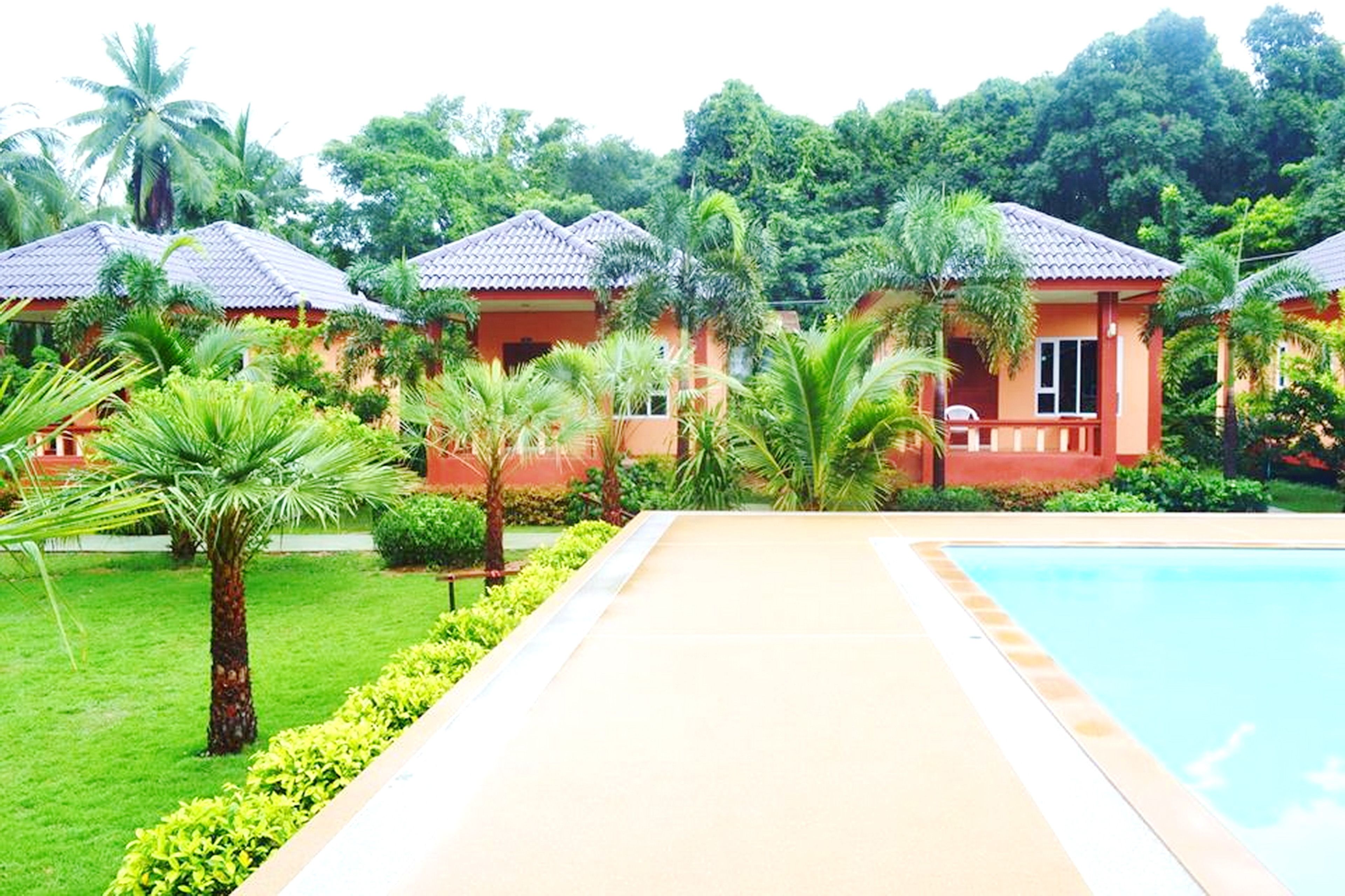 A resort with multiple bungalow-style buildings, a swimming pool, and lush greenery.