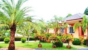 A well-maintained garden with palm trees, flowering plants, and a building with a tiled roof. - Peaceful Resort Koh Lanta (Ko Lanta)