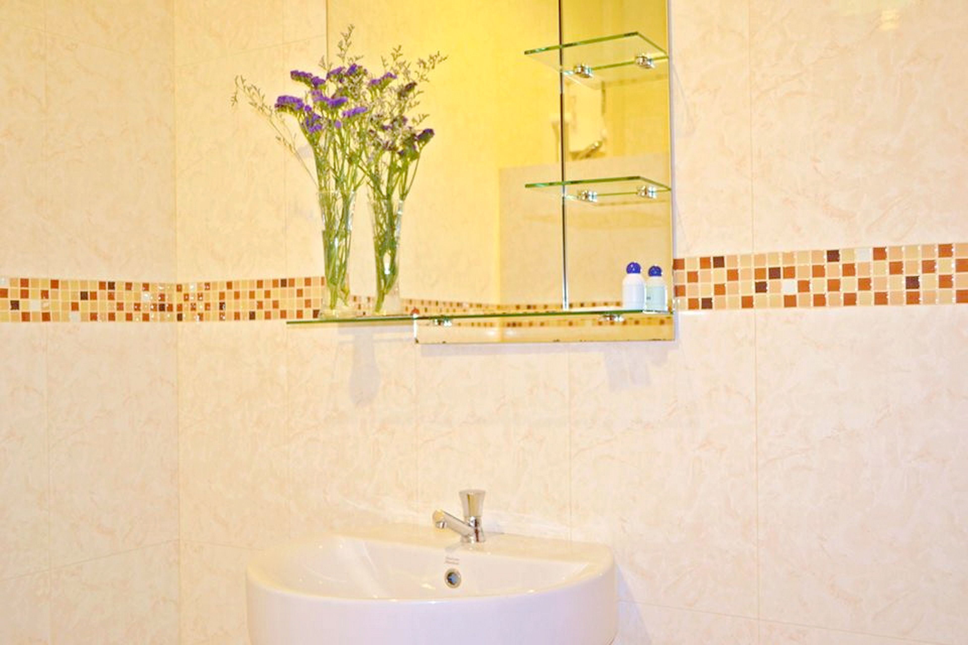 Een badkamer met een wit wastafelmeubel, een spiegel erboven en een klein plankje met toiletartikelen.