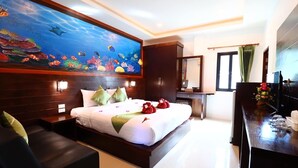 A hotel room with a large bed, a desk, a dresser, and a painting of an underwater scene. - Peaceful Resort Koh Lanta (Ko Lanta)