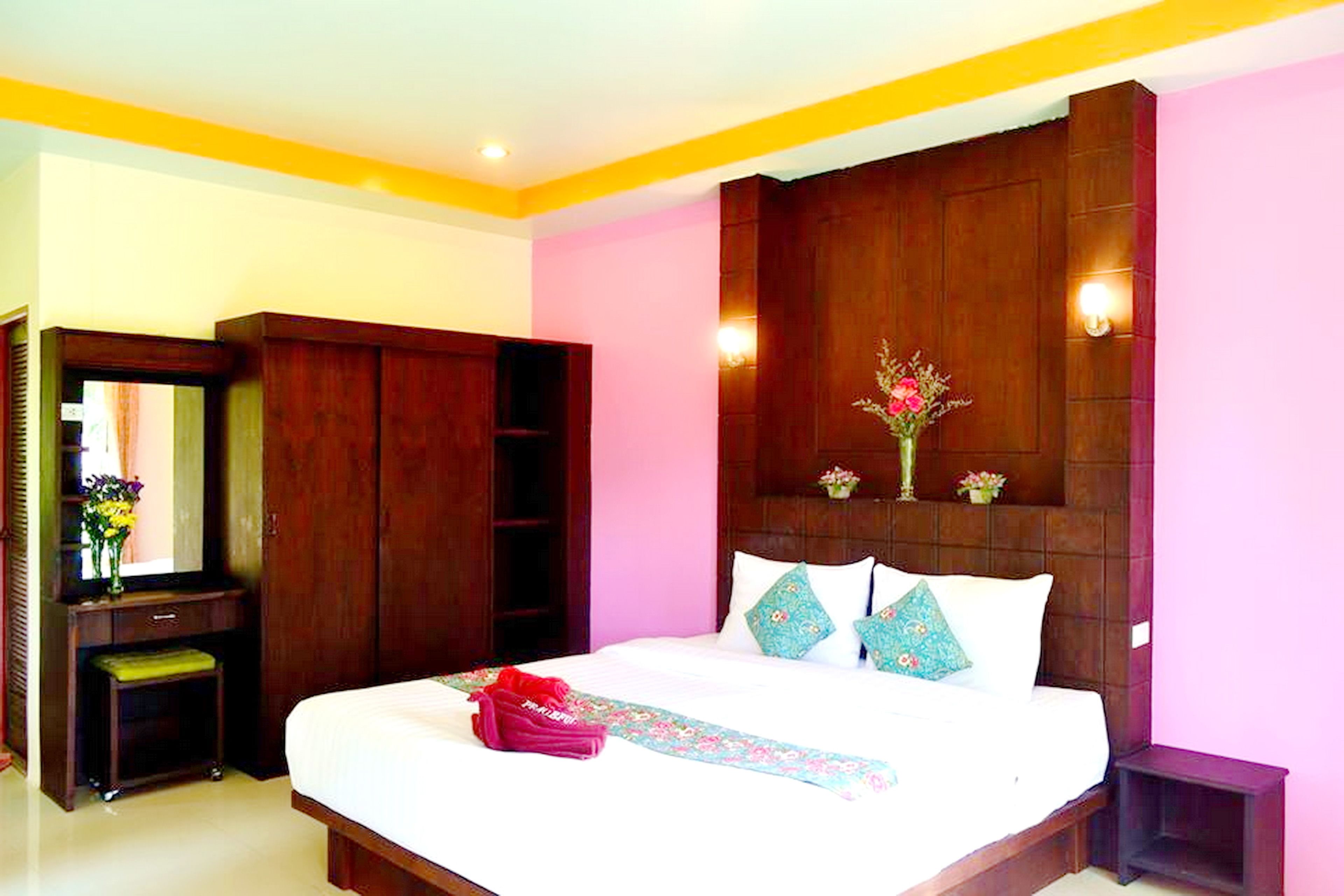 A hotel room with a large bed, wooden wardrobe, and a mirror.