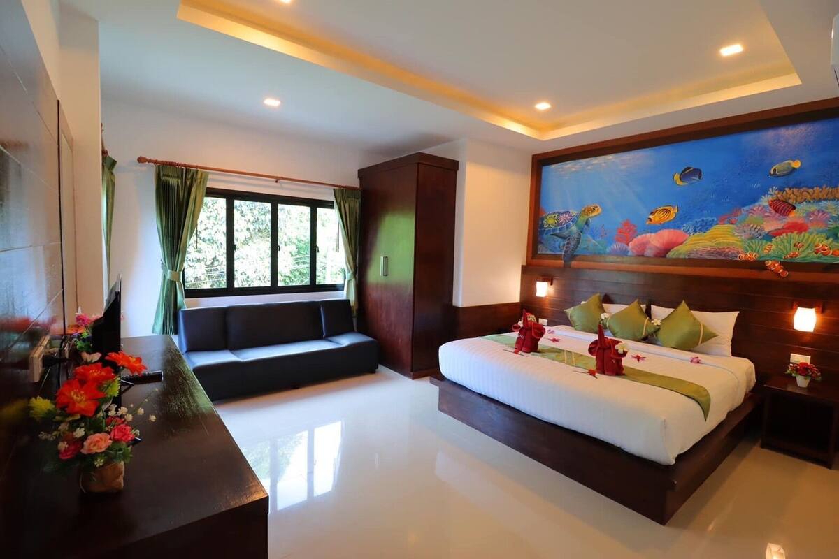 Une chambre d’hôtel avec un grand lit, un canapé, un tableau représentant des poissons et une fenêtre avec des rideaux.