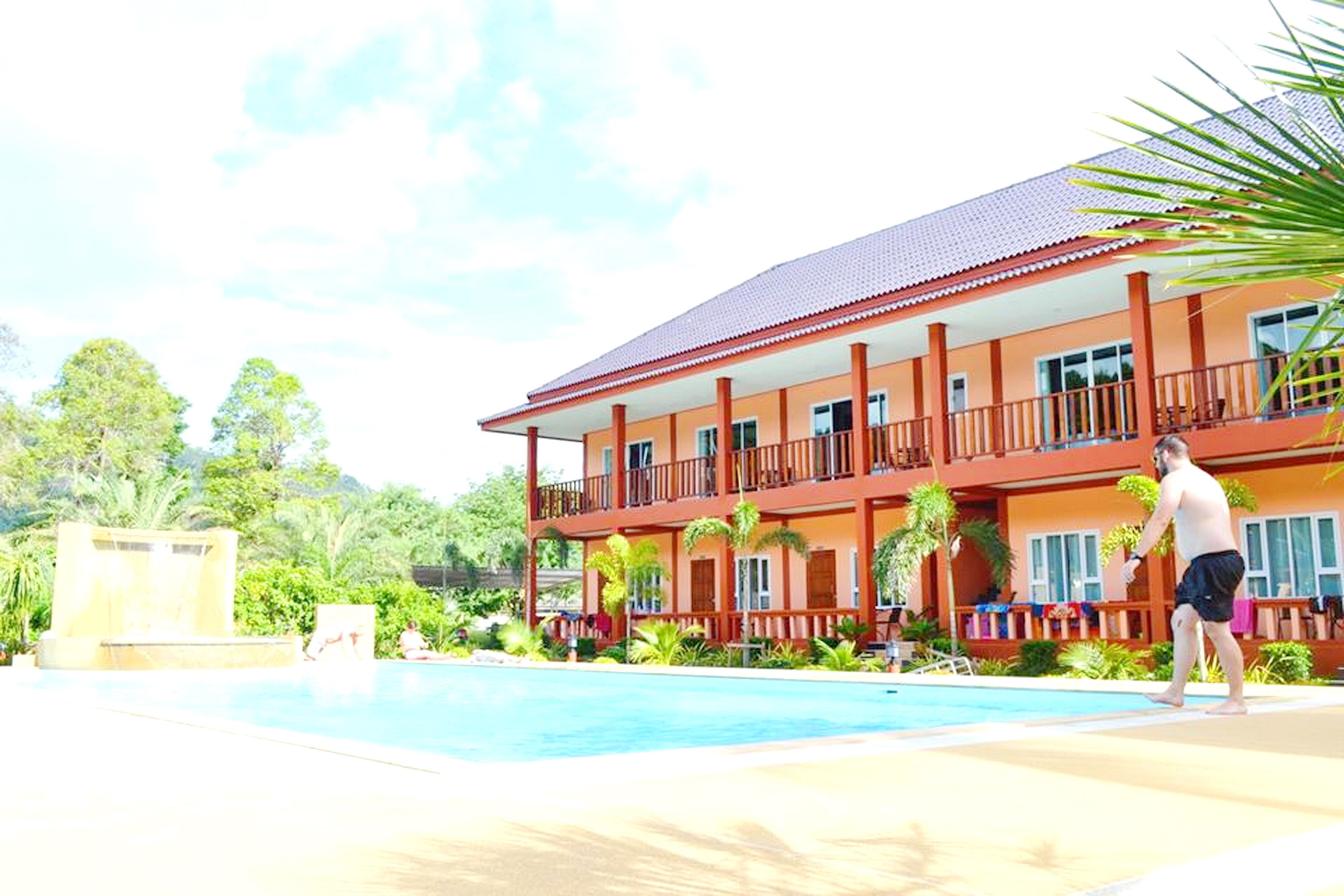 A hotel with a swimming pool, a two-story building, and a tropical garden.