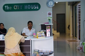 A reception desk at The City House with a clock, a no smoking sign, and a vase with flowers. - The City House (Krabi)