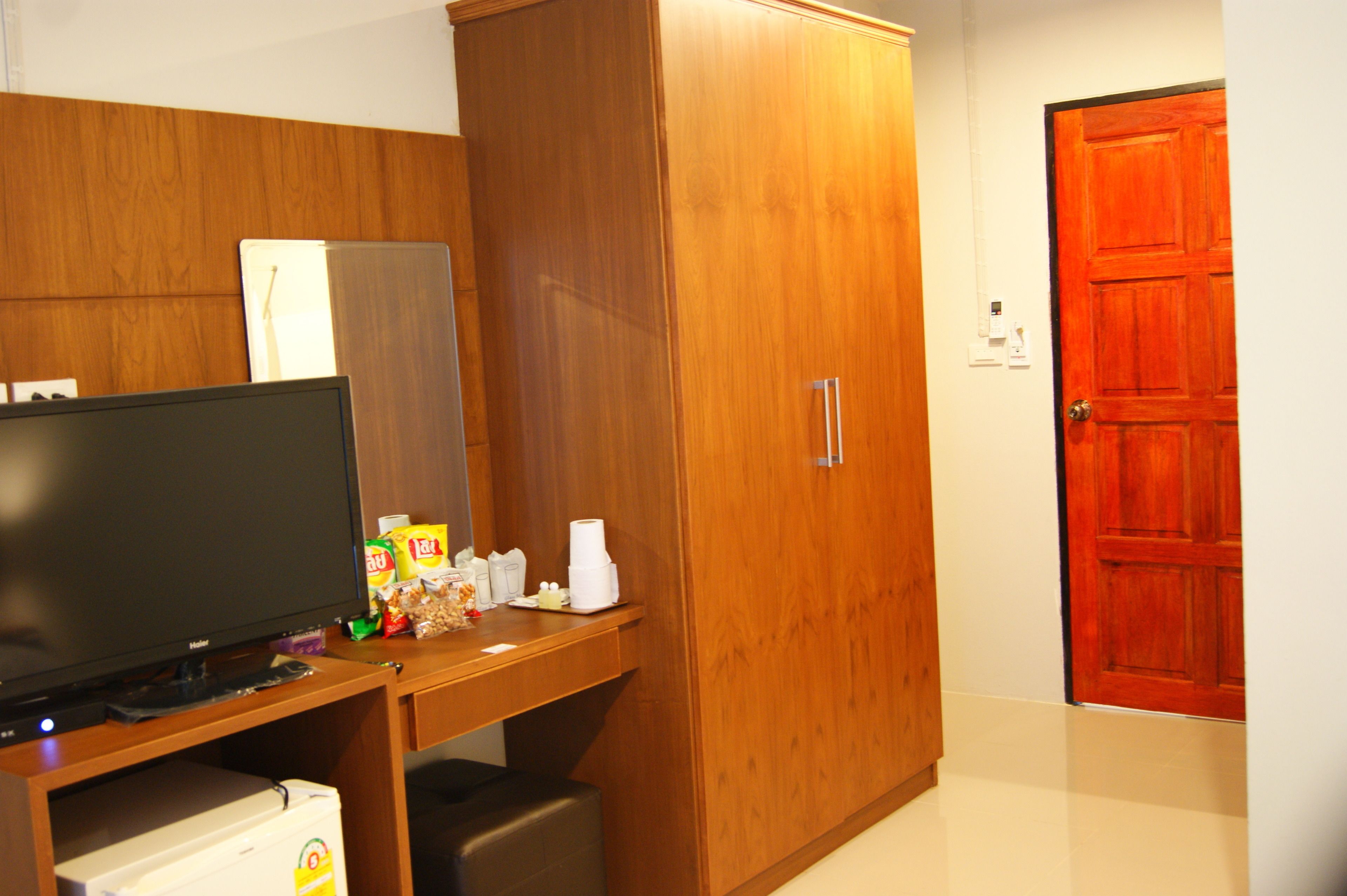 A room with a wooden wardrobe, a television, and a red door.