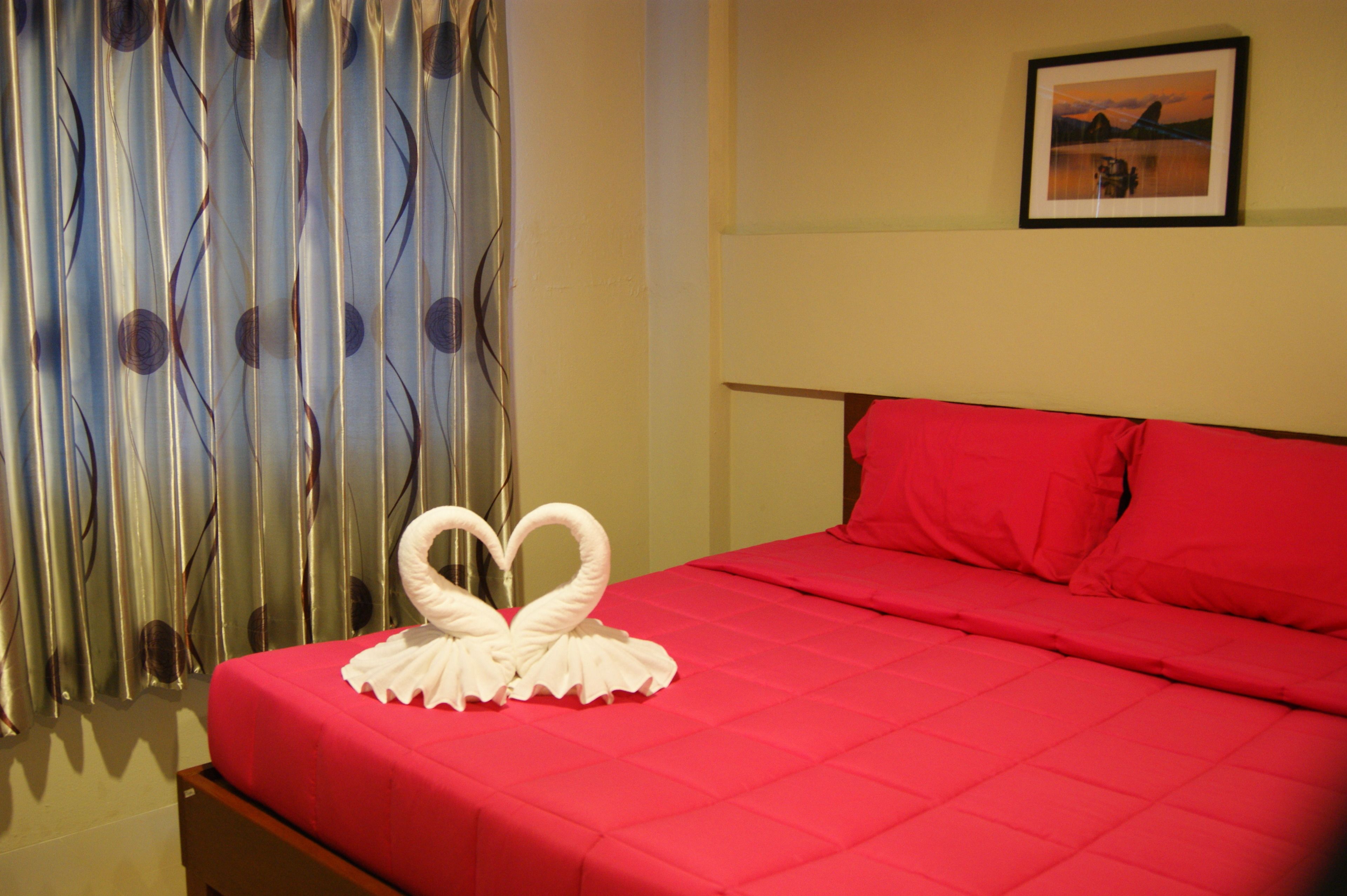 A hotel room with a red bedspread, a heart-shaped towel decoration, and a framed picture on the wall.