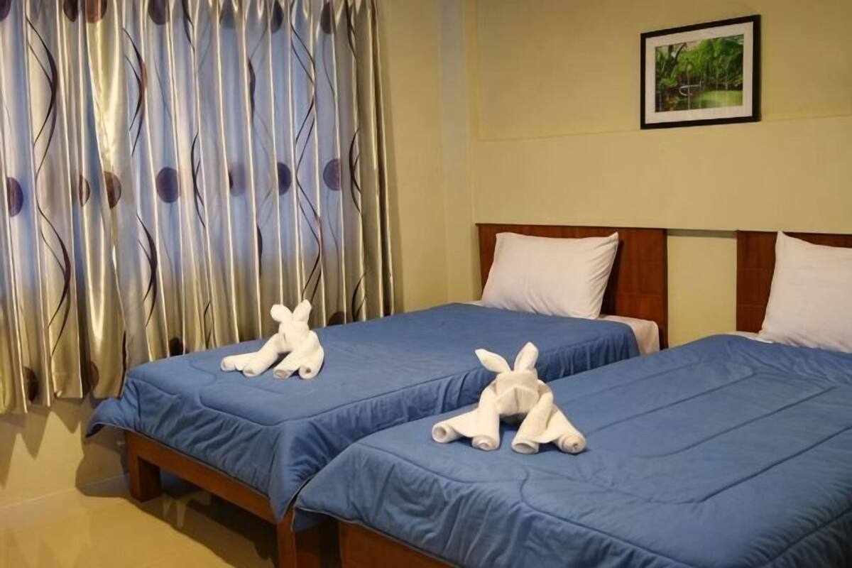 Dos camas con ropa de cama azul, un cabecero de madera y una cortina con estampado de hojas.