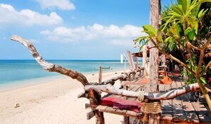 Estructura de madera frente a la playa con un banco y una hamaca, con vista a una playa arenosa y al océano.