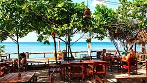 Ein Café im Freien mit Holztischen und -stühlen mit Blick auf einen Strand.