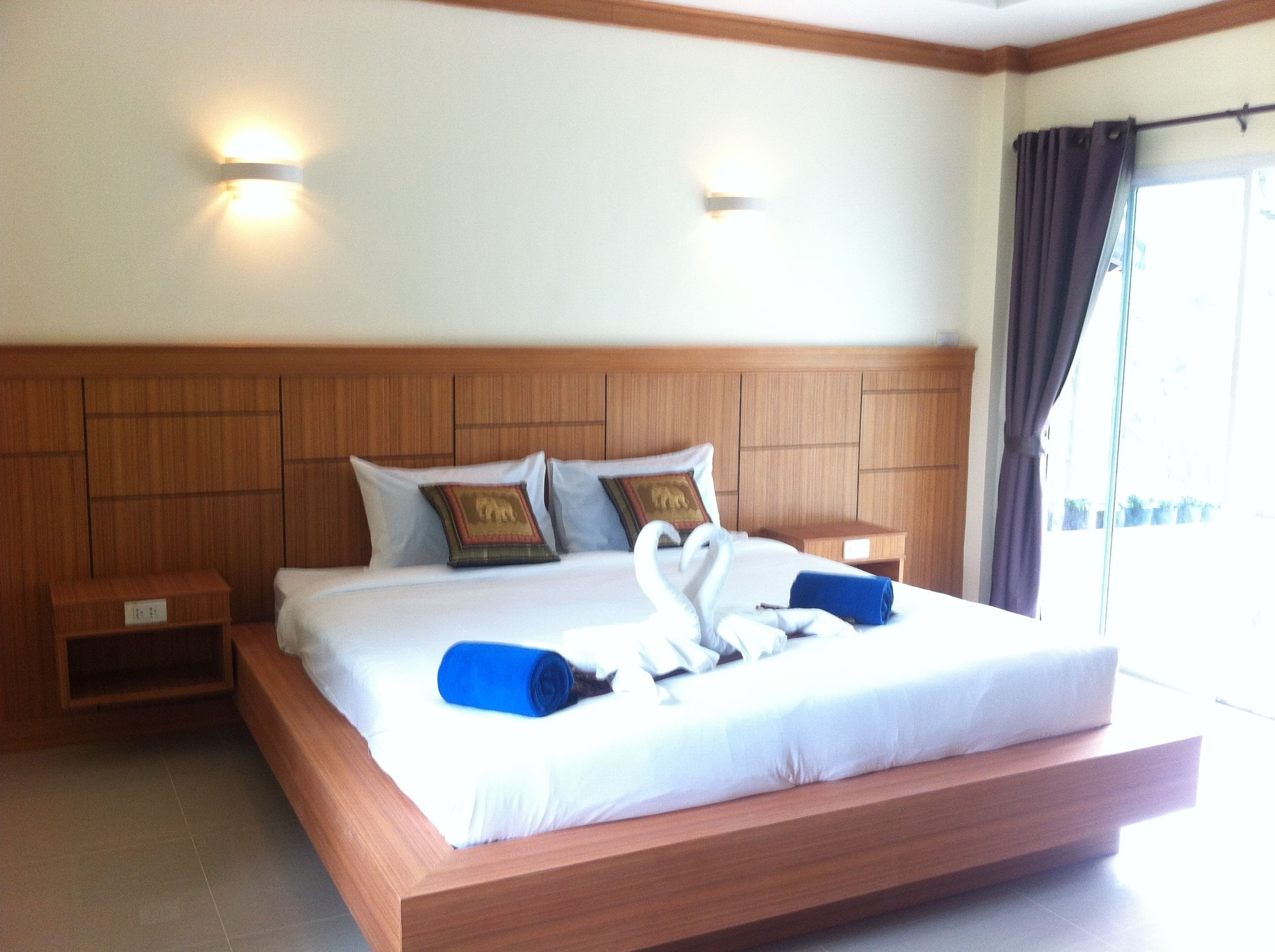 A hotel room with a large bed, wooden headboard, two bedside tables, and wall-mounted lights.