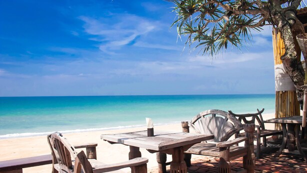 Una mesa y sillas de madera en un patio de ladrillo con vistas a la playa.