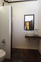 Un baño con un inodoro blanco, un lavabo con espejo y baldosas de color marrón oscuro en el suelo.