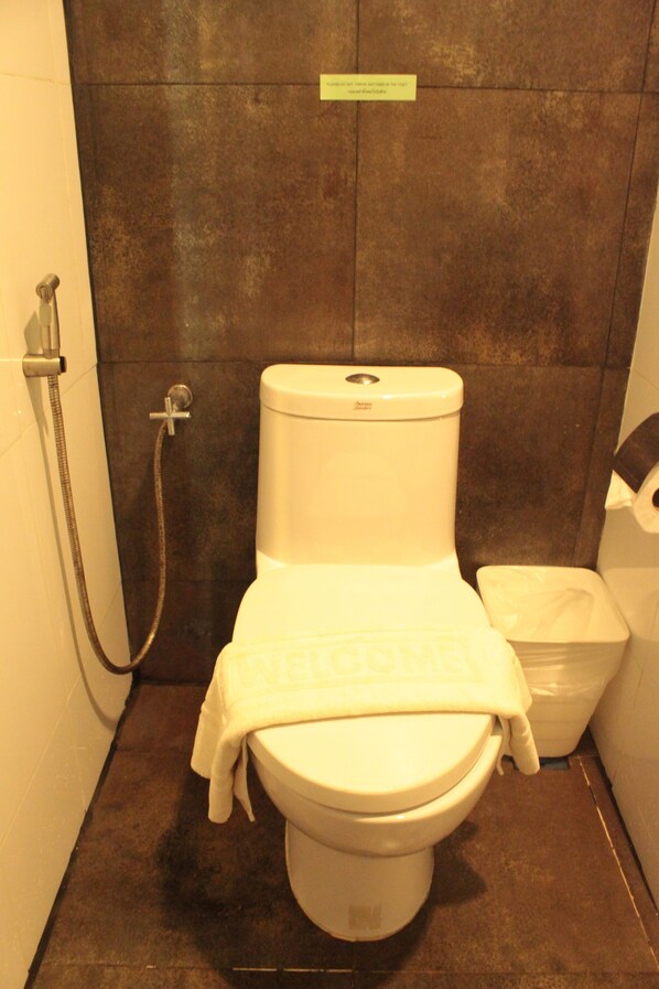 A small bathroom with a toilet, a shower, and a trash bin.