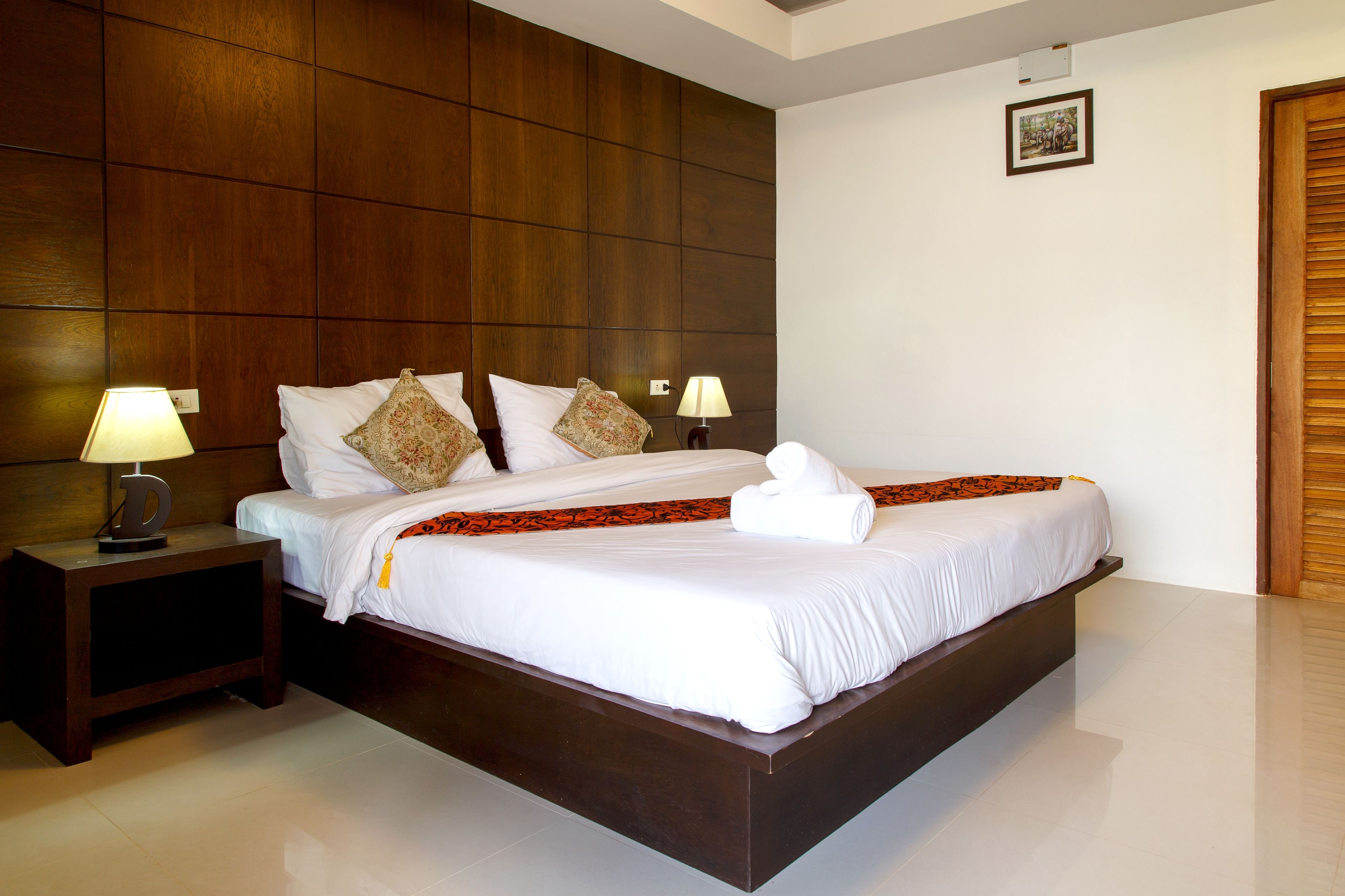A neatly made bed with white linens and a decorative throw, flanked by two bedside lamps on a wooden nightstand.