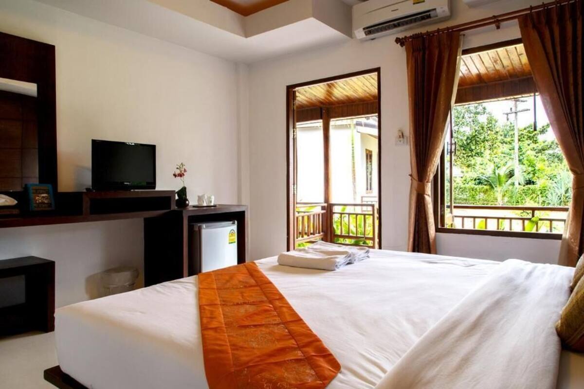 Une chambre d’hôtel équipée d’un lit, d’une télévision, d’un bureau, d’un petit réfrigérateur et d’une fenêtre avec des rideaux.