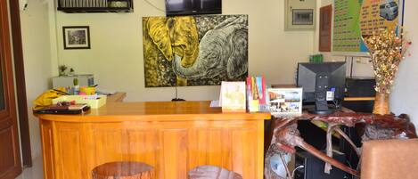 A reception desk with a wooden finish, a mounted television, and a large elephant painting on the wall.