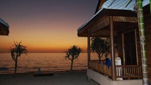 Een strandhut met een houten dak en balkon, met uitzicht op de oceaan tijdens de zonsondergang.