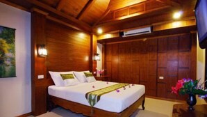 Een bed met houten frame, witte beddengoed en een groene loper, een nachtkastje met een lamp, en een houten garderobe.