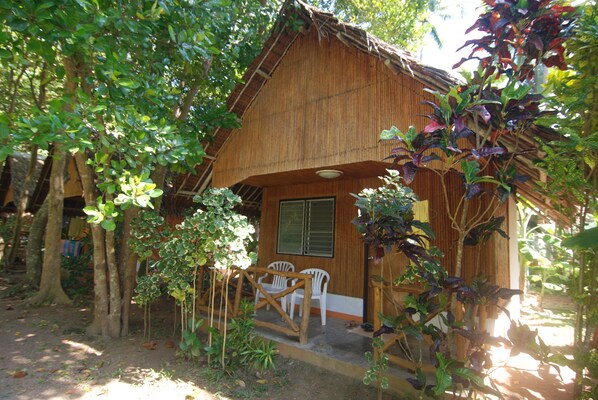 A rustic wooden house with a thatched roof, surrounded by lush greenery and trees. - Lanta Coral Beach Resort (Ko Lanta)