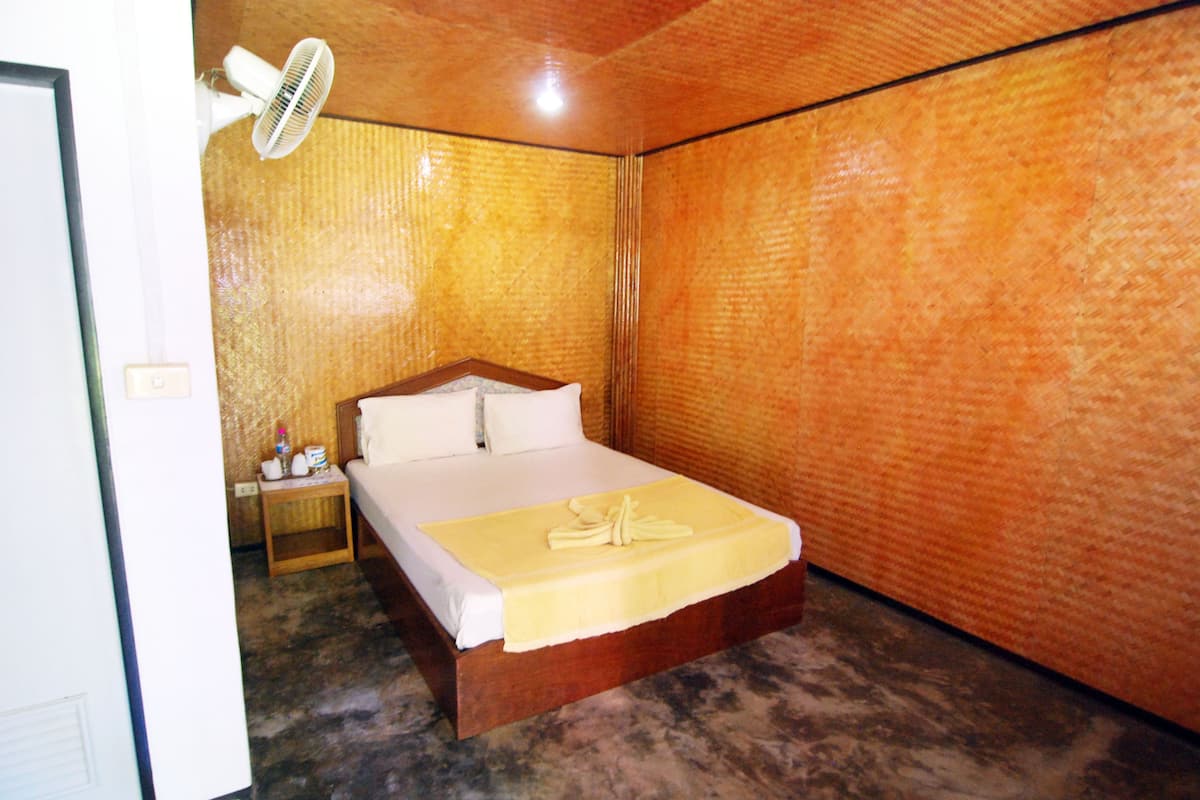 Een kamer met een bed, nachtkastje, ventilator en een muur met een structuur.