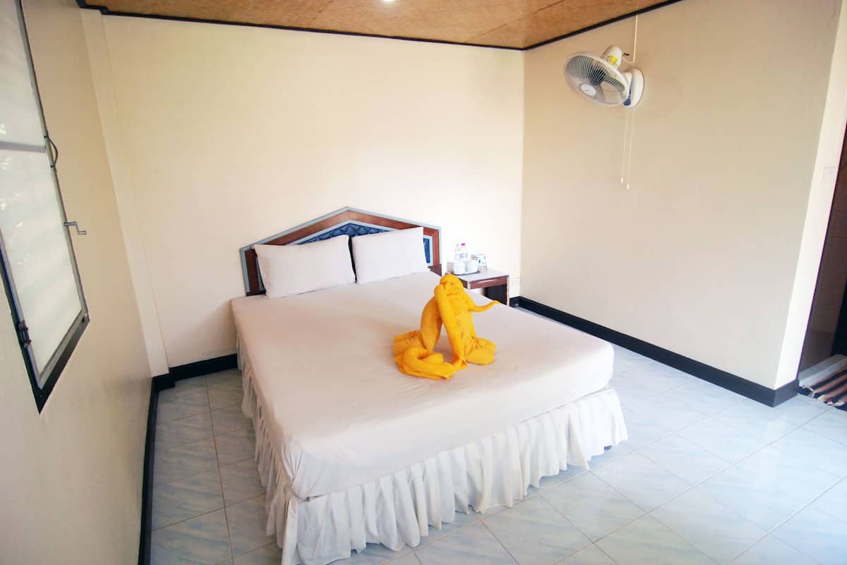 Een hotelkamer met een groot bed, een nachtkastje met een ventilator en een raam met luxaflex.