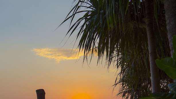 Een hangmat op een strand, met een zonsondergang op de achtergrond.