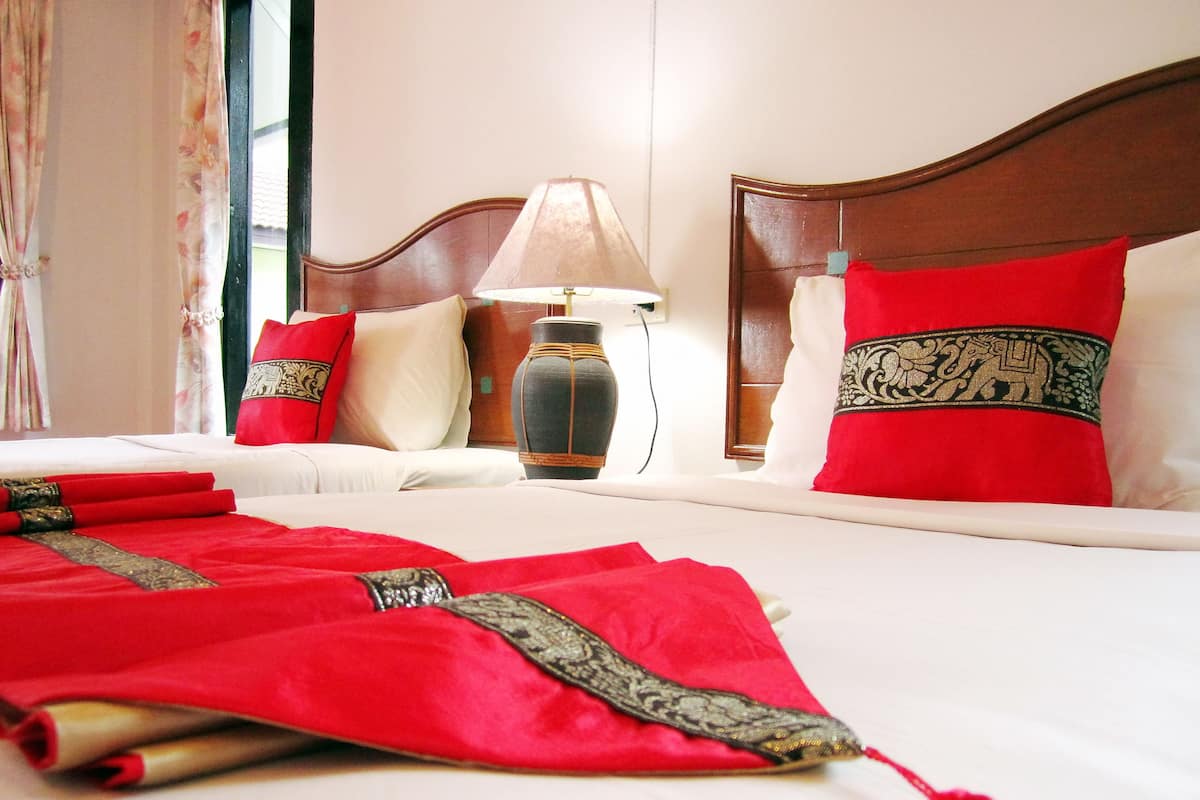 Una cama bien tendida con ropa de cama roja y blanca, una lámpara y un florero en la mesita de noche.
