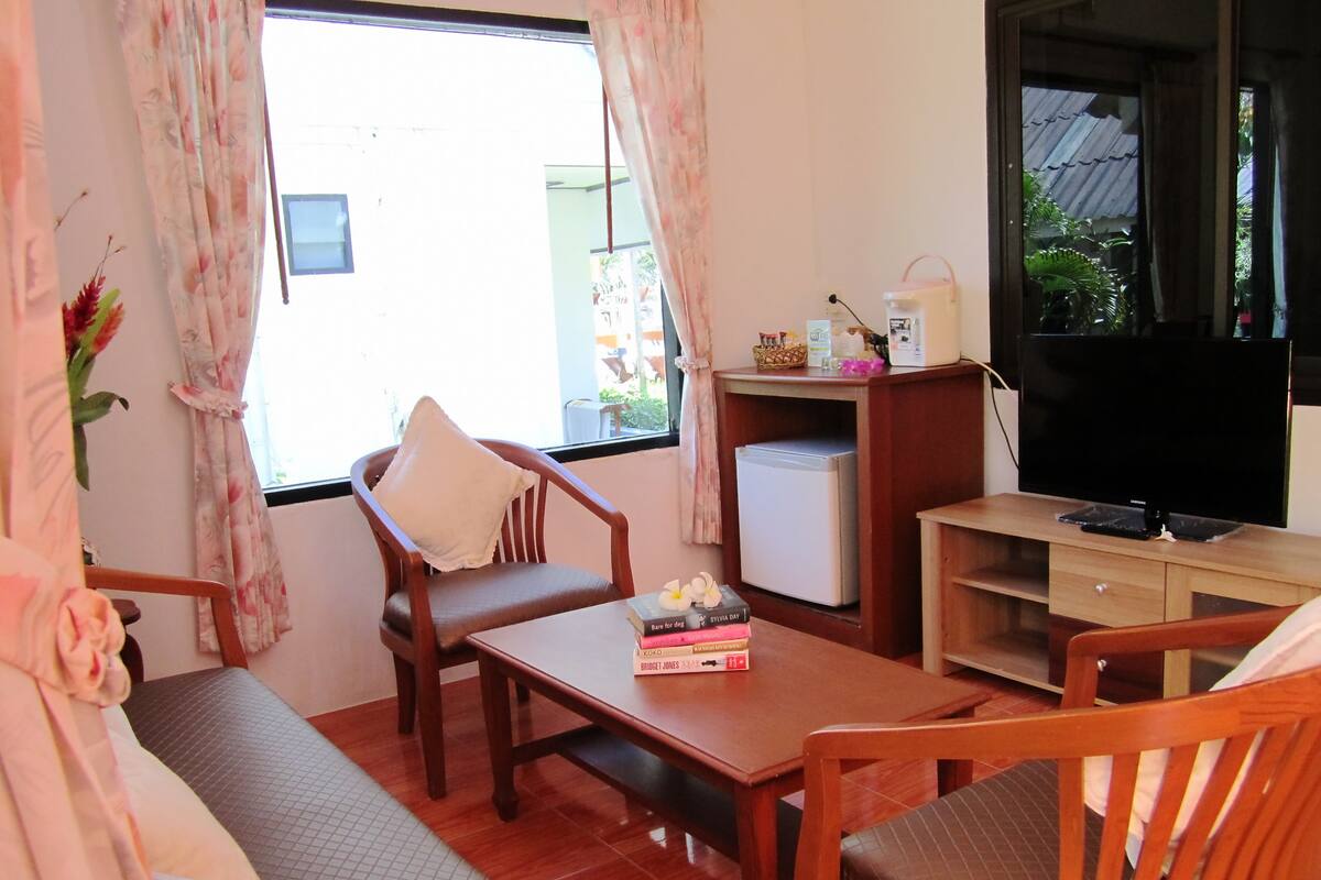 Una sala de estar acogedora con sofá, sillas de madera, una mesa de centro, televisor y refrigerador.